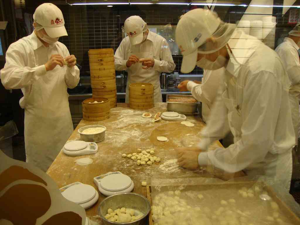 You can watch the master chefs making the dumplings through glass! They are incredibly methodical: one person rolls the dough, the next adds the filling, and the final chef folds it with a perfectly precise serrated edge!