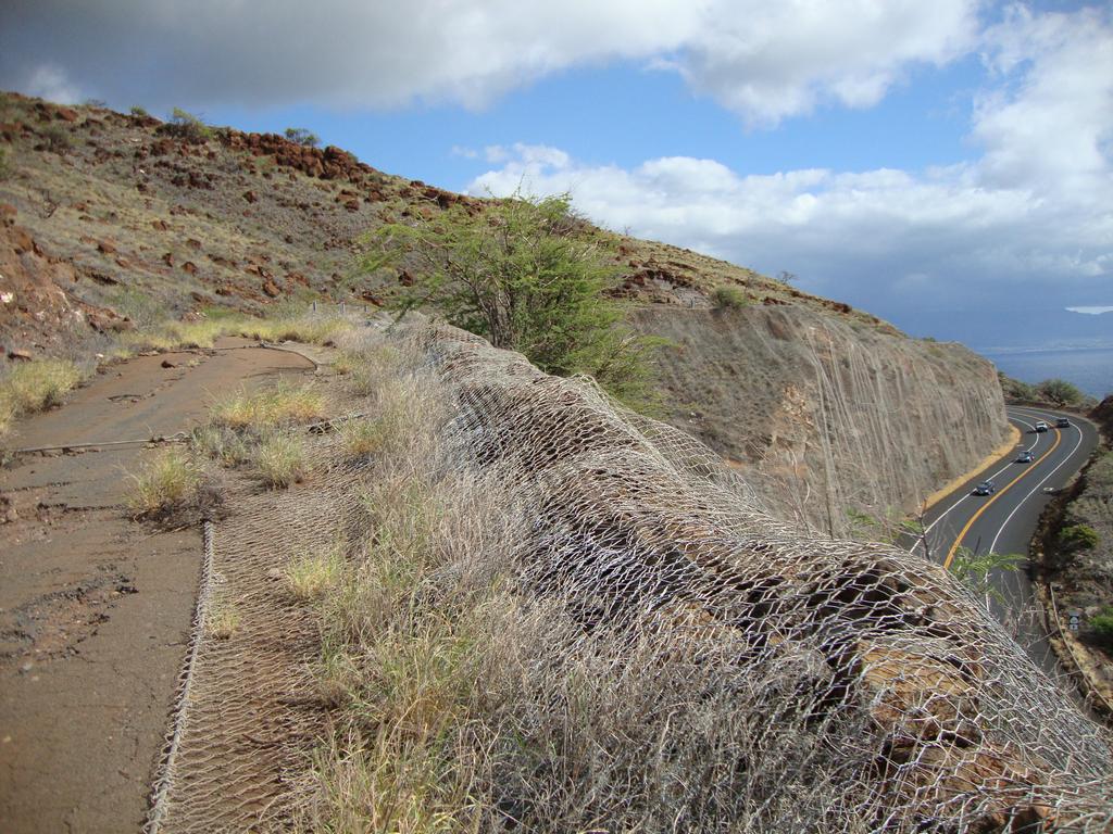 The old road to Lahaina is on the left and the new road is on the right. The view is looking toward Kihei. The chain-link fencing is to keep falling rocks off the new road.